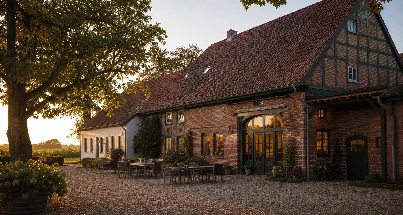 Ein restaurierter westfälischer Ziegelhof mit Tischen unter einer alten Kastanie am frühen Abend